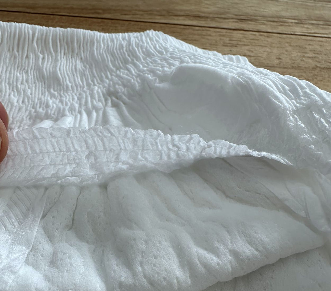 Close view of the back of a nappy pant, with the gathered lip of the back pocket standing away from the surface