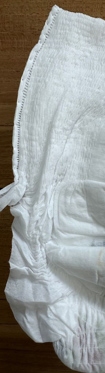 The bonded side seam running down the edge of a nappy pant, with the tear tab at the bottom of it